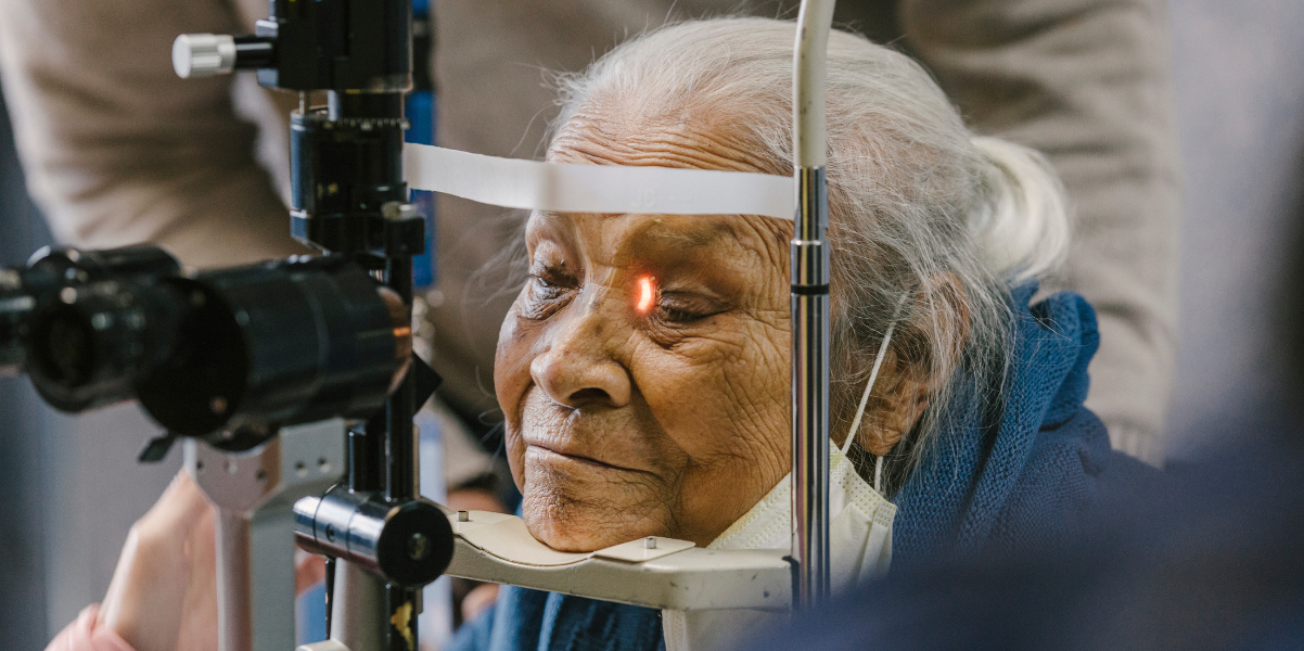 An older woman rests her chin on a machine as she receives an eye exam as part of PRASAD's eye care donation program.